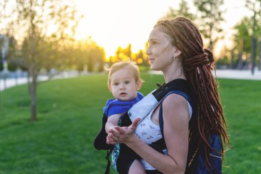 Genç mutlu anne bebek oğlu ile ergo birlikte seyahat etmek sırt çantası. Güneşli yaz günü. Modern anne kavramı