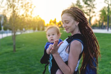 Genç Anne Bebek oğlu ile ergo sırt çantası mutlu parkta oynuyorlar. Güneşli yaz günü. Modern anne kavramı
