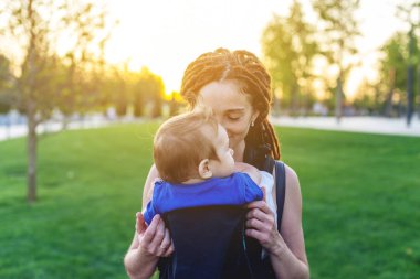 Genç mutlu anne bebek oğlu ile ergo sırt çantası Park'ta yürüyordunuz. Güneşli yaz günü. Modern anne kavramı