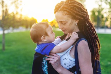 Genç mutlu anne bebek oğlu ile ergo birlikte seyahat etmek sırt çantası. Güneşli yaz günü. Modern anne kavramı