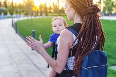 Genç mutlu anne bebek oğlu ile ergo birlikte seyahat etmek sırt çantası. Güneşli yaz günü parkta. Modern anne kavramı