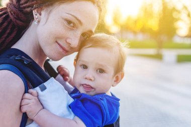 Genç mutlu anne bebek oğlu ile ergo sırt çantası Park'ta yürüyordunuz. Güneşli yaz günü. Modern anne kavramı