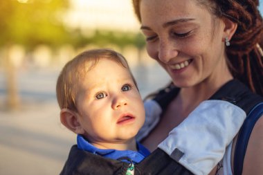 Genç mutlu anne bebek oğlu ile ergo sırt çantası Park'ta yürüyordunuz. Güneşli yaz günü. Modern anne kavramı