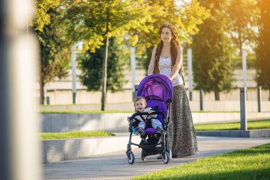 Sunny Park'ta yürüyordunuz bebek arabası bebek oğluyla genç modern anne. Sevinç annelik ve Sonbahar ruh kavramı