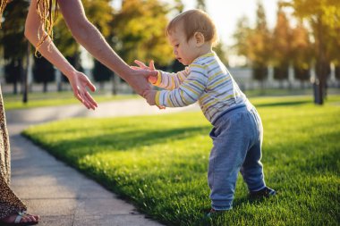Anne şirin bebek sonbahar günü yeşil çim üzerinde bir Sunny doğada yürüyüş yardımcı olur. Kavramı ilk çocuk adımları