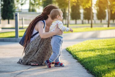 Anne şirin bebek sonbahar günü yeşil çim üzerinde bir Sunny doğada yürüyüş yardımcı olur. Kavramı ilk çocuk adımları
