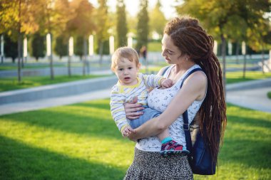 Genç modern mutlu anne ile bebek evlat Sunny Park'ta yürüyordunuz. Sevinç annelik ve Sonbahar ruh kavramı