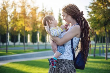Genç modern mutlu anne ile bebek evlat Sunny Park'ta yürüyordunuz. Sevinç annelik ve Sonbahar ruh kavramı