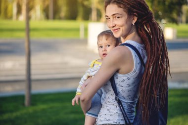 Genç modern mutlu anne ile bebek evlat Sunny Park'ta yürüyordunuz. Sevinç annelik ve Sonbahar ruh kavramı