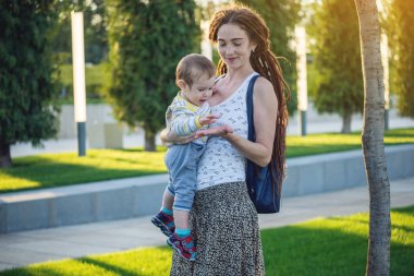 Genç modern mutlu anne ile bebek evlat Sunny Park'ta yürüyordunuz. Sevinç annelik ve Sonbahar ruh kavramı