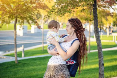 Genç modern mutlu anne ile bebek evlat Sunny Park'ta yürüyordunuz. Sevinç annelik ve Sonbahar ruh kavramı