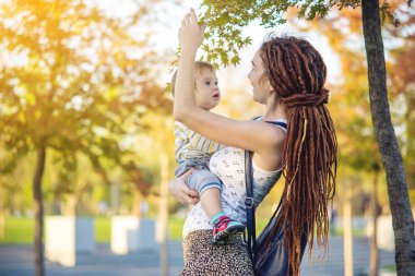 Genç modern mutlu anne ile bebek evlat Sunny Park'ta yürüyordunuz. Sevinç annelik ve Sonbahar ruh kavramı
