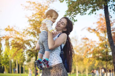 Genç modern mutlu anne ile bebek evlat Sunny Park'ta yürüyordunuz. Sevinç annelik ve Sonbahar ruh kavramı
