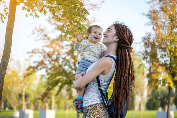 Young modern happy mom with baby son walking in Sunny Park. The concept of the joy of motherhood and autumn mood