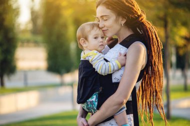 Genç modern mutlu anne ile bebek evlat Sunny Park'ta yürüyordunuz. Sevinç annelik ve Sonbahar ruh kavramı