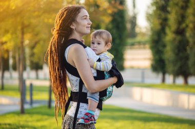 Genç modern mutlu anne ile bebek evlat Sunny Park'ta yürüyordunuz. Sevinç annelik ve Sonbahar ruh kavramı