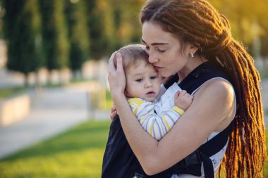 Genç modern mutlu anne bebek oğlu ile ergo sırt çantası içinde güneşli yaz günü yürüyüş. Annelik sevinci kavramı