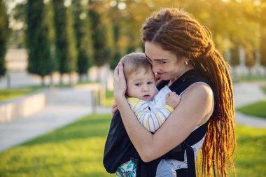 Genç modern mutlu anne bebek oğlu ile ergo sırt çantası içinde güneşli yaz günü yürüyüş. Annelik sevinci kavramı