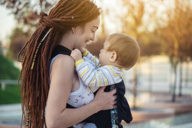 Genç modern mutlu anne bebek oğlu ile ergo sırt çantası içinde güneşli yaz günü yürüyüş. Annelik sevinci kavramı