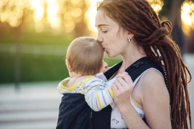 Genç modern mutlu anne bebek oğlu ile ergo sırt çantası içinde güneşli yaz günü yürüyüş. Annelik sevinci kavramı