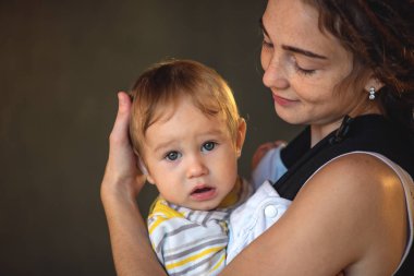 Mutlu anne bebek oğlu ile ergo sırt çantası arka planda karanlık duvara portre genç. Modern anne kavramı