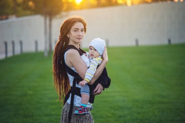 Genç modern mutlu anne bebek oğlu ile ergo sırt çantası içinde güneşli yaz günü yürüyüş. Annelik sevinci kavramı