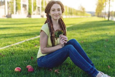 Elma yeme ve sonbahar güneşli ruh zevk yeşil çayır üzerinde parkta bir saç modeli dreadlocks ile modern genç kız