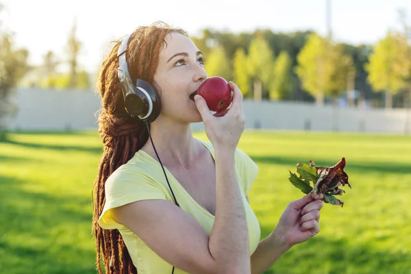 Beautiful modern woman listening to music with her headphones on the background of nature in autumn Sunny Park. The concept of good mood, favorite music, happy time.