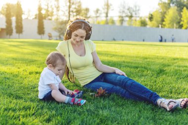 Yeşil bir çayırda şirin bebek oğluyla bir Sunny parkta oynarken güzel genç modern anne. Annelik sevinci kavramı
