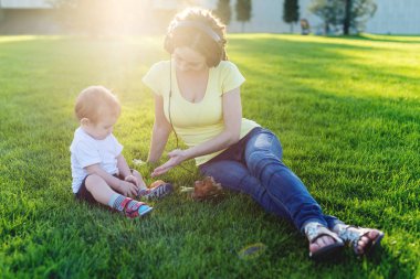 Yeşil bir çayırda şirin bebek oğluyla bir Sunny parkta oynarken güzel genç modern anne. Annelik sevinci kavramı