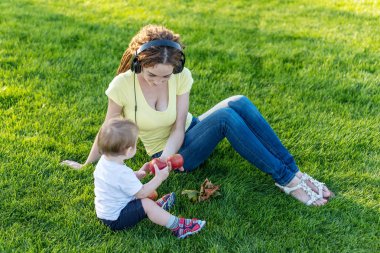 Yeşil bir çayırda şirin bebek oğluyla bir Sunny parkta oynarken güzel genç modern anne. Annelik sevinci kavramı