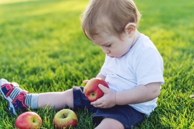 Güneşli bir günde elma doğada yeşil bir çimenlikte oynamaktan şirin bebek. Bir yaşındaki çocuk kavramı