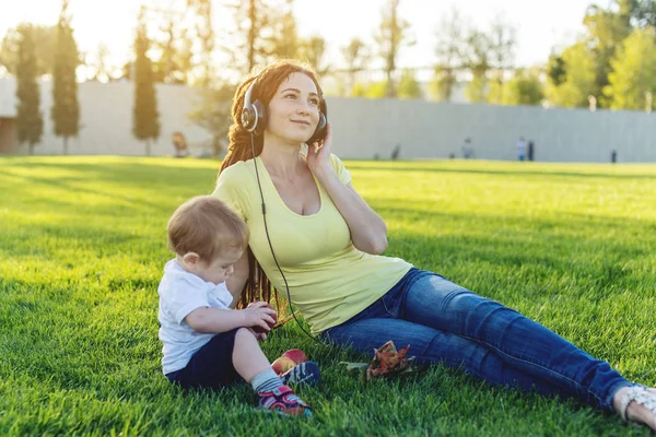 Beautiful young modern mom playing in a green meadow with her cute baby son in a Sunny Park. The concept of the joy of motherhood