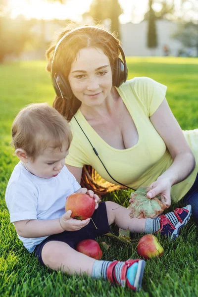 Beautiful young modern mom playing in a green meadow with her cute baby son in a Sunny Park. The concept of the joy of motherhood