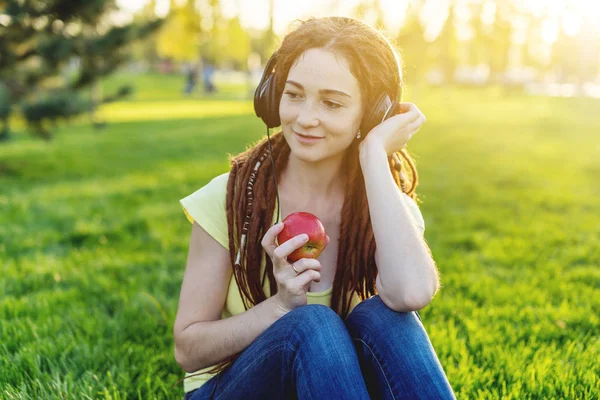 Beautiful modern woman listening to music with her headphones on the background of nature in autumn Sunny Park. The concept of Melomania and good mood