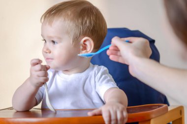 Küçük çocuk çocuk mutfakta çocuk masasında yemeye öğrenir. Bir kaşığı yulaf lapası elini uzatarak anne beslemeleri