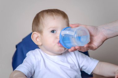 Küçük bebek çocuk mutfakta bir sandalyede otururken İçmesuyu. Onun elinde bir plastik şişe uzatarak anne