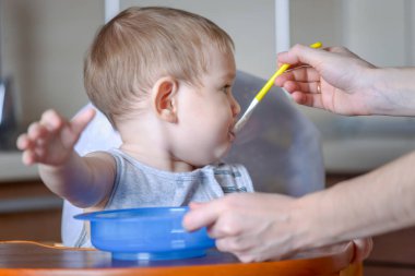 Küçük çocuk çocuk mutfakta çocuk masasında yemeye öğrenir. Bir kaşığı yulaf lapası elini uzatarak anne beslemeleri