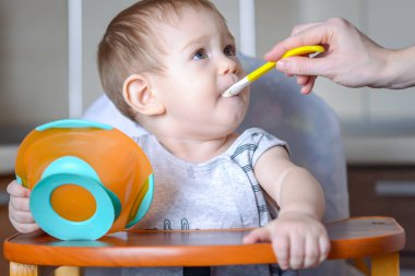 Küçük çocuk çocuk mutfakta çocuk masasında yemeye öğrenir. Bir kaşığı yulaf lapası elini uzatarak anne beslemeleri