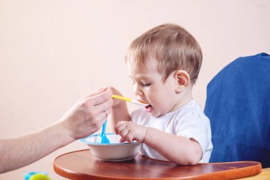 Bir iskemle mutfakta yemek küçük şirin bebeğim. Anne elinde tutan bir kaşık yulaf lapası beslemeleri