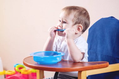 Plastik kaşık kemiren küçük şirin çocuk. Çocuklar masada yemek öğrenen bebek