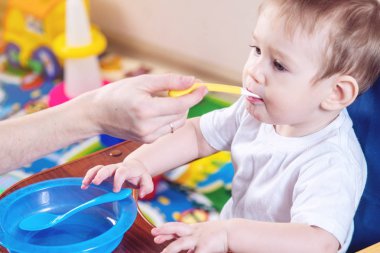 Bir iskemle mutfakta yemek küçük şirin bebeğim. Anne elinde tutan bir kaşık yulaf lapası beslemeleri