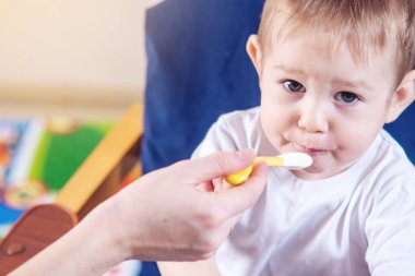 Bir iskemle mutfakta yemek küçük şirin bebeğim. Anne elinde tutan bir kaşık yulaf lapası beslemeleri