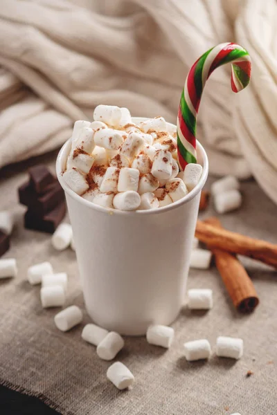 A mug of hot chocolate with marshmallow on top and a Lollipop stick on a knitted blanket background. Cozy warm winter rustic mood composition