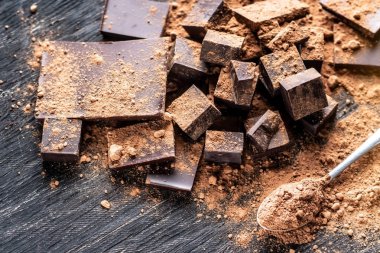 Koyu ahşap zemin üzerine kakao tozu ile karanlık bitter çikolata parçaları. Şekerleme malzemeler kavramı