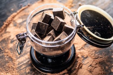 Ahşap arka plan üzerinde bir cam kavanoza kakao tozu ile karanlık bitter çikolata parçaları. Şekerleme malzemeler kavramı