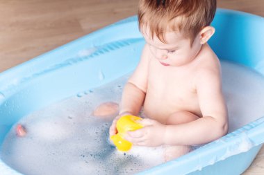 Şirin bebek çocuk mavi banyo banyo yıkama. Çocuk bir sarı ördek ve sabun köpüğü ile oynuyor.