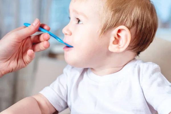 stock image Mom feeding the baby holding out her hand with a spoon of food in the kitchen. Healthy baby nutrition. The emotions of a child while eating