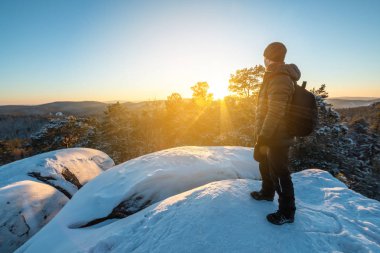 Bir sırt çantası ile adam uzun yürüyüşe çıkan kimse günbatımında Sibirya ormanları içinde bir uçurumun üstünde duruyor. Yaban hayatı güzel kar Panoraması. Özgürlük ve kış trekking