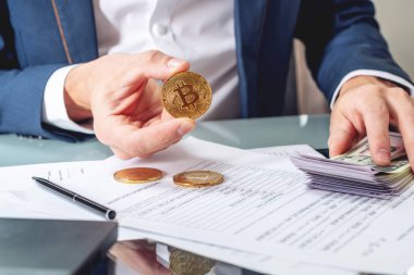 Bir madeni para bitcoin tutan belgelerle masada oturan işadamı bankacı. Exchange ve cryptocurrency dolar satışı kavramı